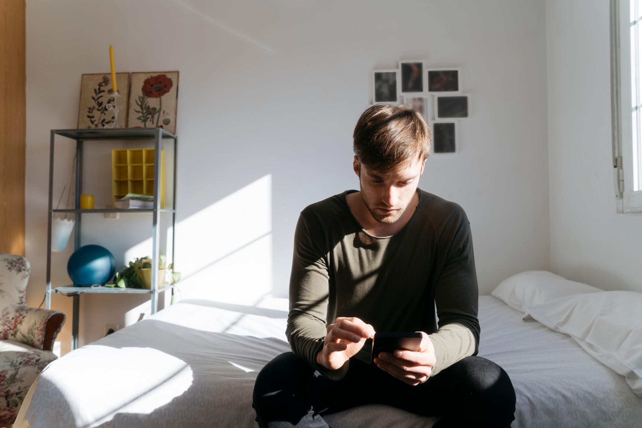 Anxious-man-alone-at-bedroom-using-his-phone-current-unemployment-rate