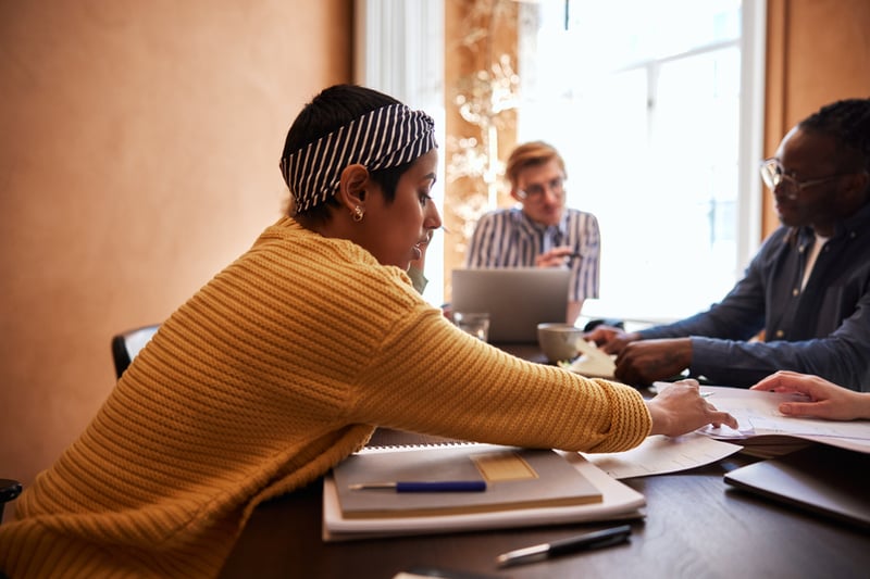 image-woman-sitting-across-colleagues-reaching-for-a-paper-on-a-table-experiential-learning
