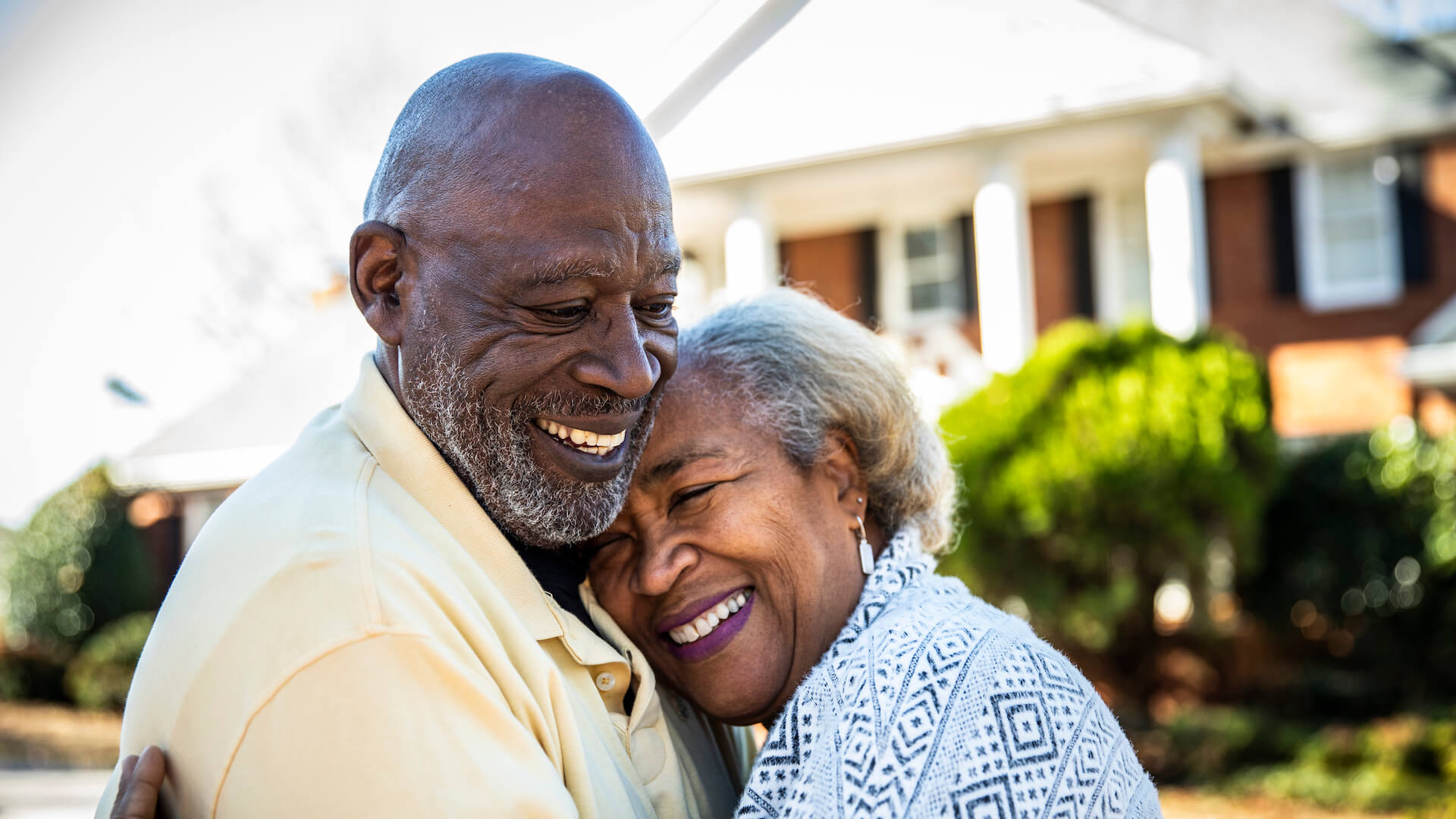 financial-security-older-couple-hugging-in-front-of-home