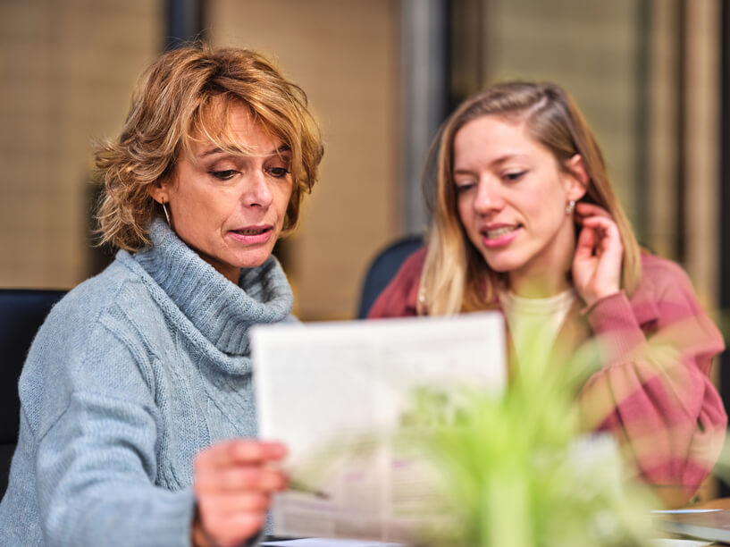 two-female-employees-discussing-a-document-micromanaging-boss