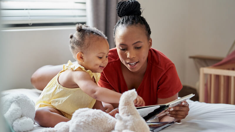 parenting-styles-mom-lays-on-bed-with-baby-and-book