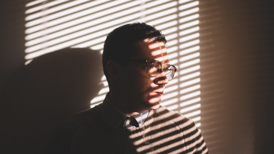 support-employee-mental-health-person-looks-through-blinds-light-on-face