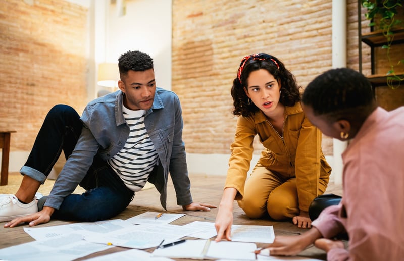 group-of-people-sit-on-the-floor-around-papers-team-empowerment