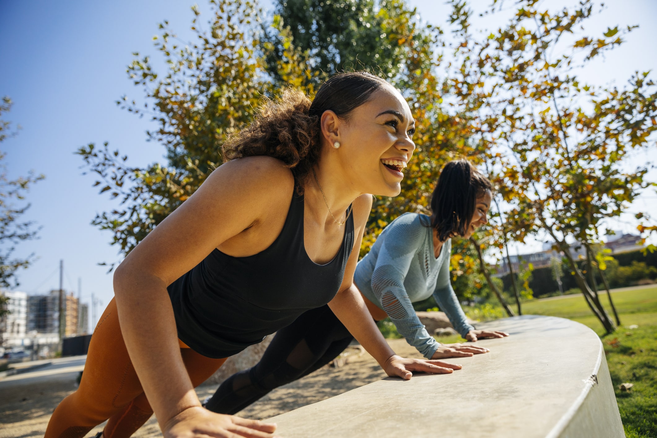 Cheerful-women-doing-push-ups-on-retaining-wall-at-park-finding-purpose-after-college