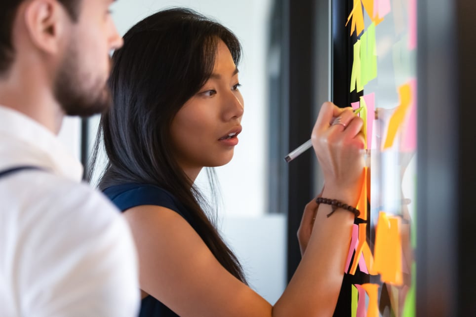 Focused-asian-woman-writing-idea-on-sticky-notes-action-verbs-for-resume