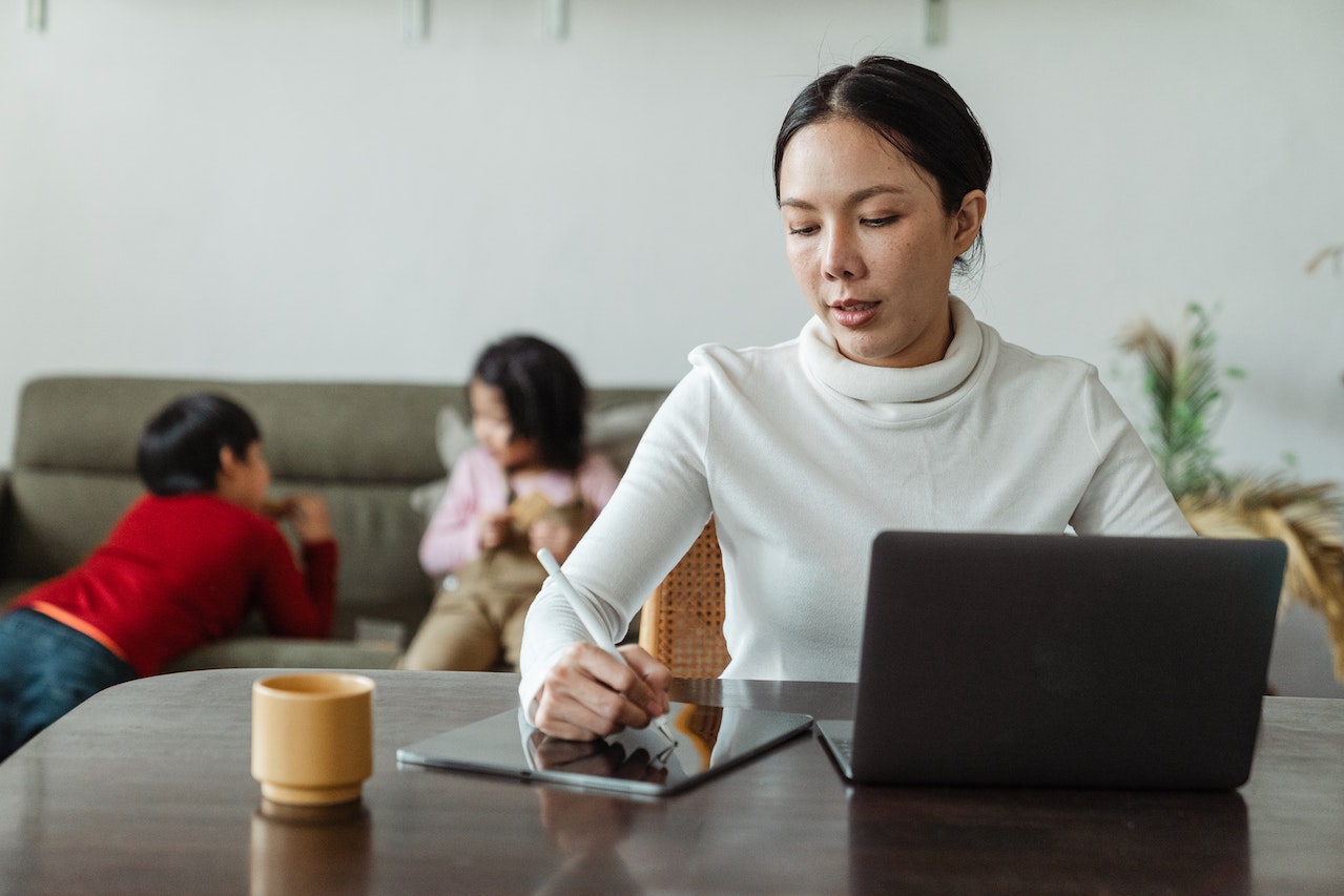 Focused-woman-writing-on-her-tablet-with-her-laptop-open-besides-her-pros-and-cons-list