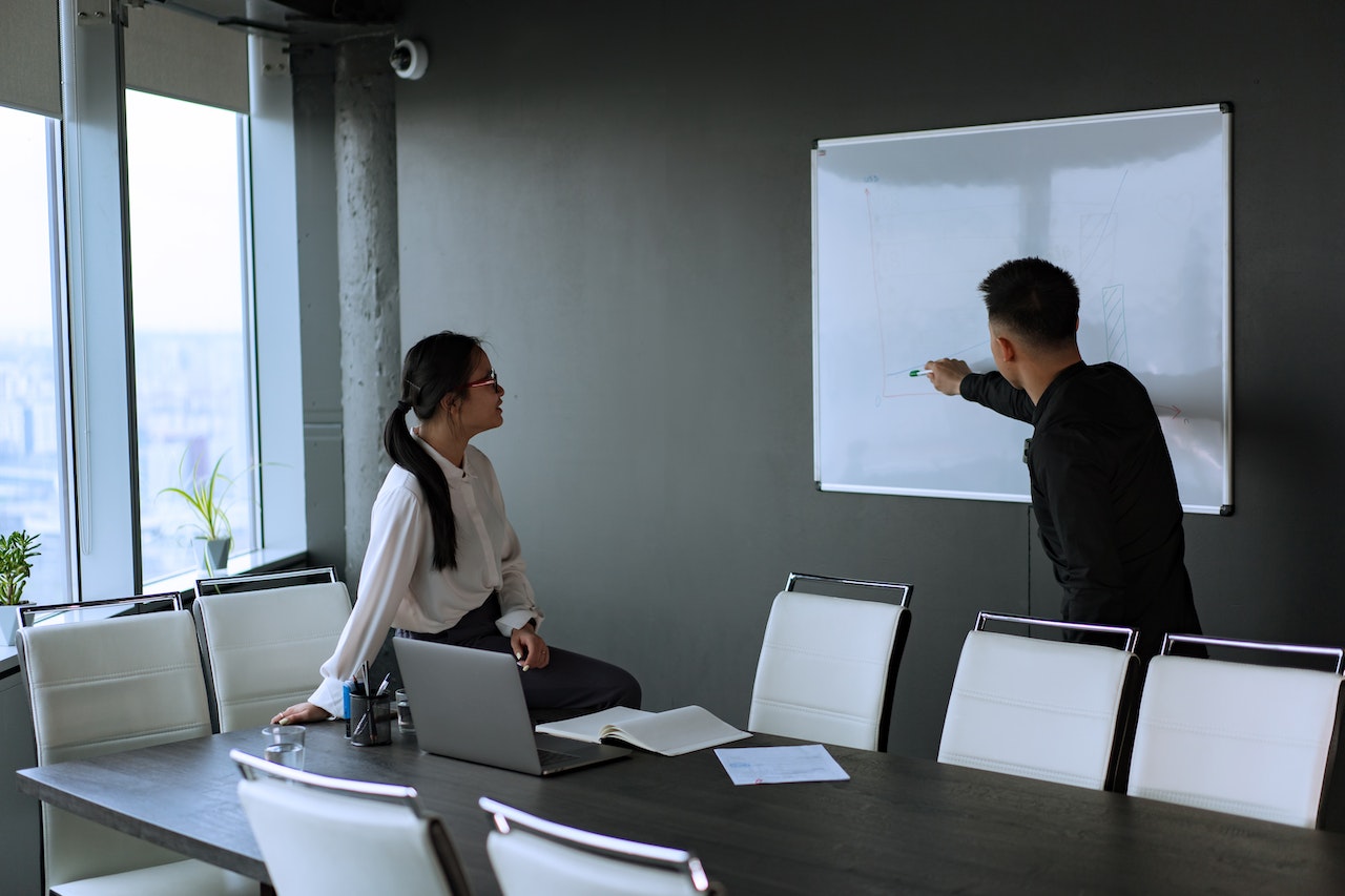 Man-and-woman-looking-and-pointing-at-whiteboard-pros-and-cons-list