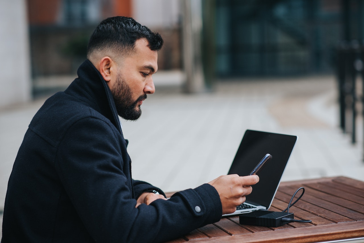 Serious-ethnic-entrepreneur-using-smartphone-at-outdoors-table-with-laptop-best-jobs-for-career-change