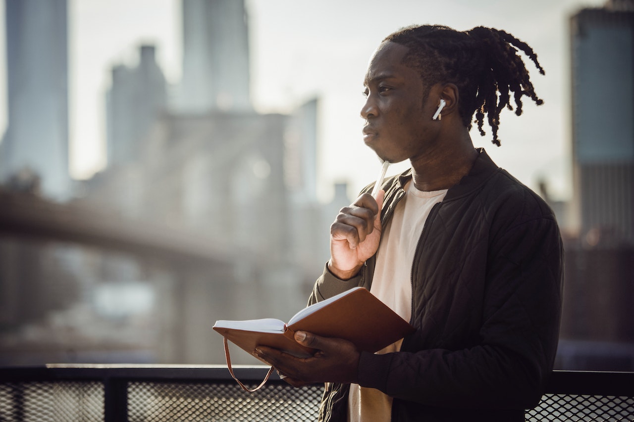 Thoughtful-man-in-wireless-earphones-with-notepad-on-balconyhow-to-get-inspired