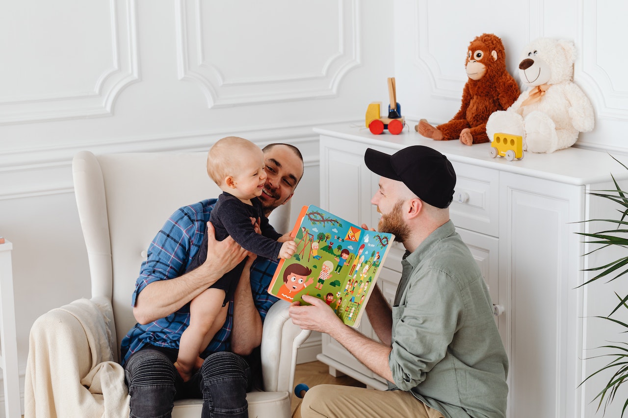 Two-men-holding-their-baby-and-reading-him-a-book-at-home-quality-time-with-family