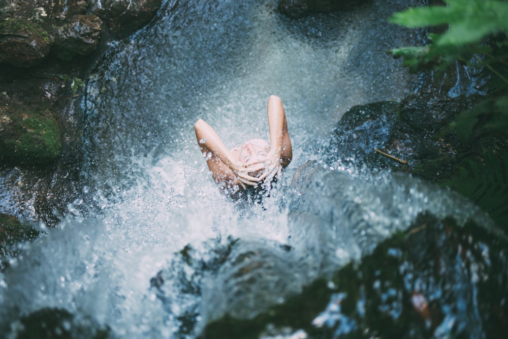 Woman-showering-on-waterfall-in-nature