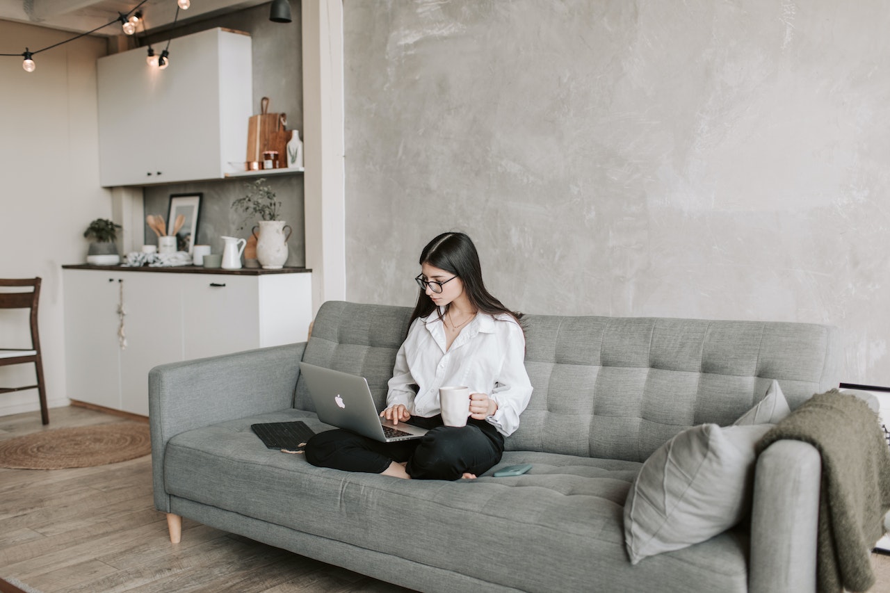 Woman-sitting-on-her-couch-working-from-laptop-with-coffee-cup-how-to-use-100-of-your-brain