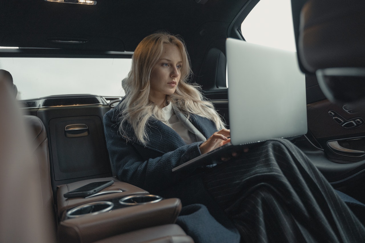 ambitious-woman-using-laptop-while-sitting-on-back-of-her-car-driven-by-chauffeur-type-b-personality