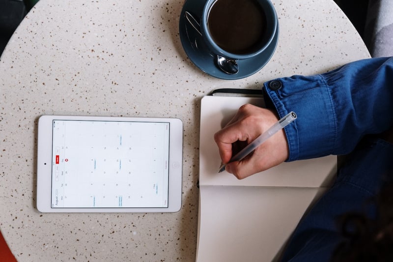 close-up-of-hands-writing-on-notebook-while-lookiing-at-calendar-on-phone-daily-schedule