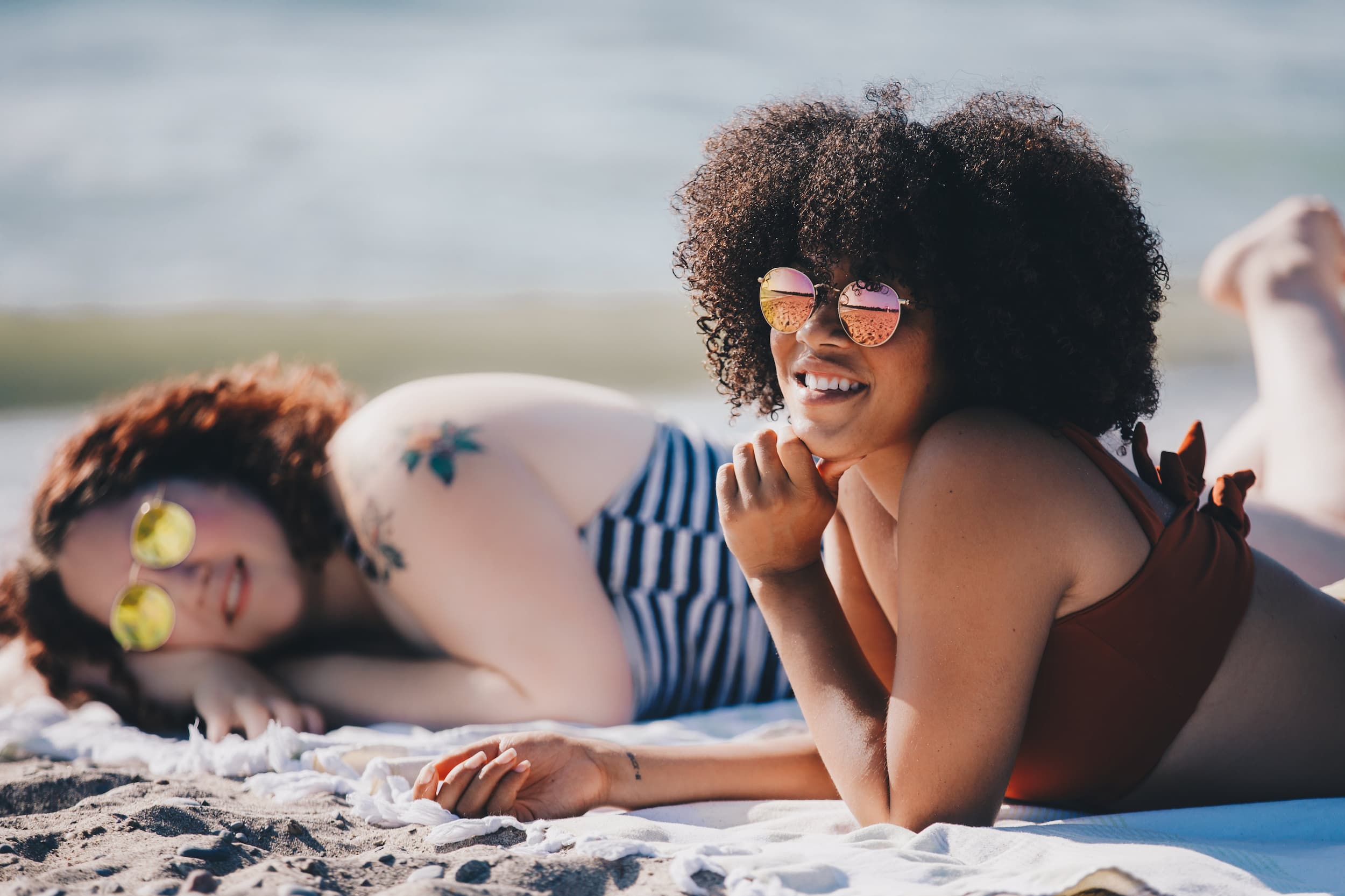 two-women-lay-on-beach-enjoying-main-character-syndrome