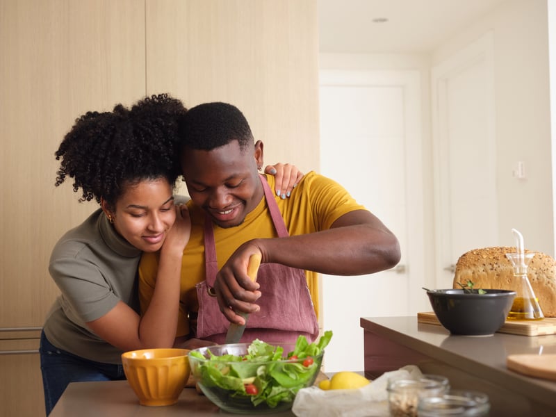 man-cutting-ingredient-for-salad-while-his-beautiful-girlfriend-embracing-him-looking-down-at-board-how-to-build-confidence