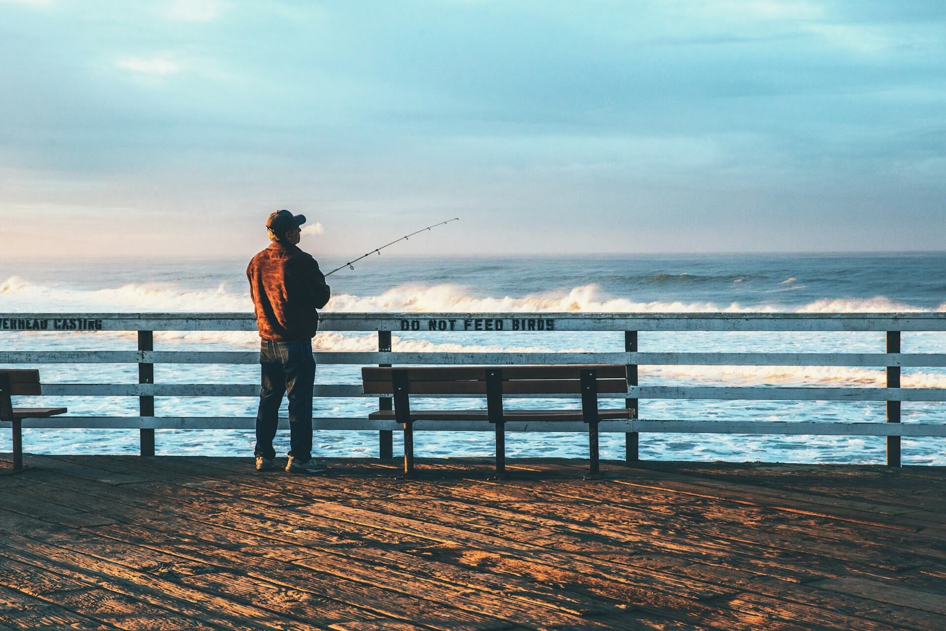 man fishin over pier in baseball cap