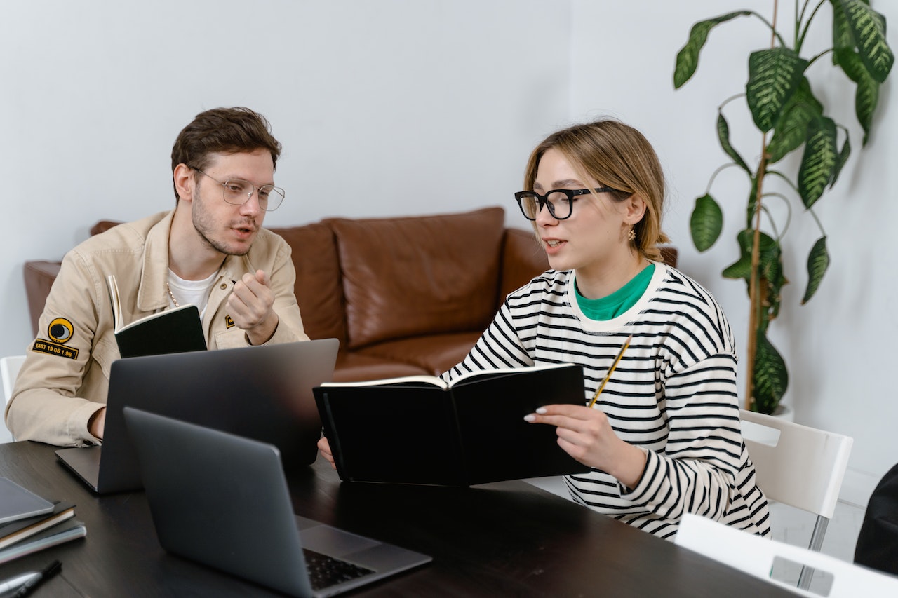 man-and-woman-at-office-looking-at-book-and-laptop-thinking-and-discussing-convergert-thinking