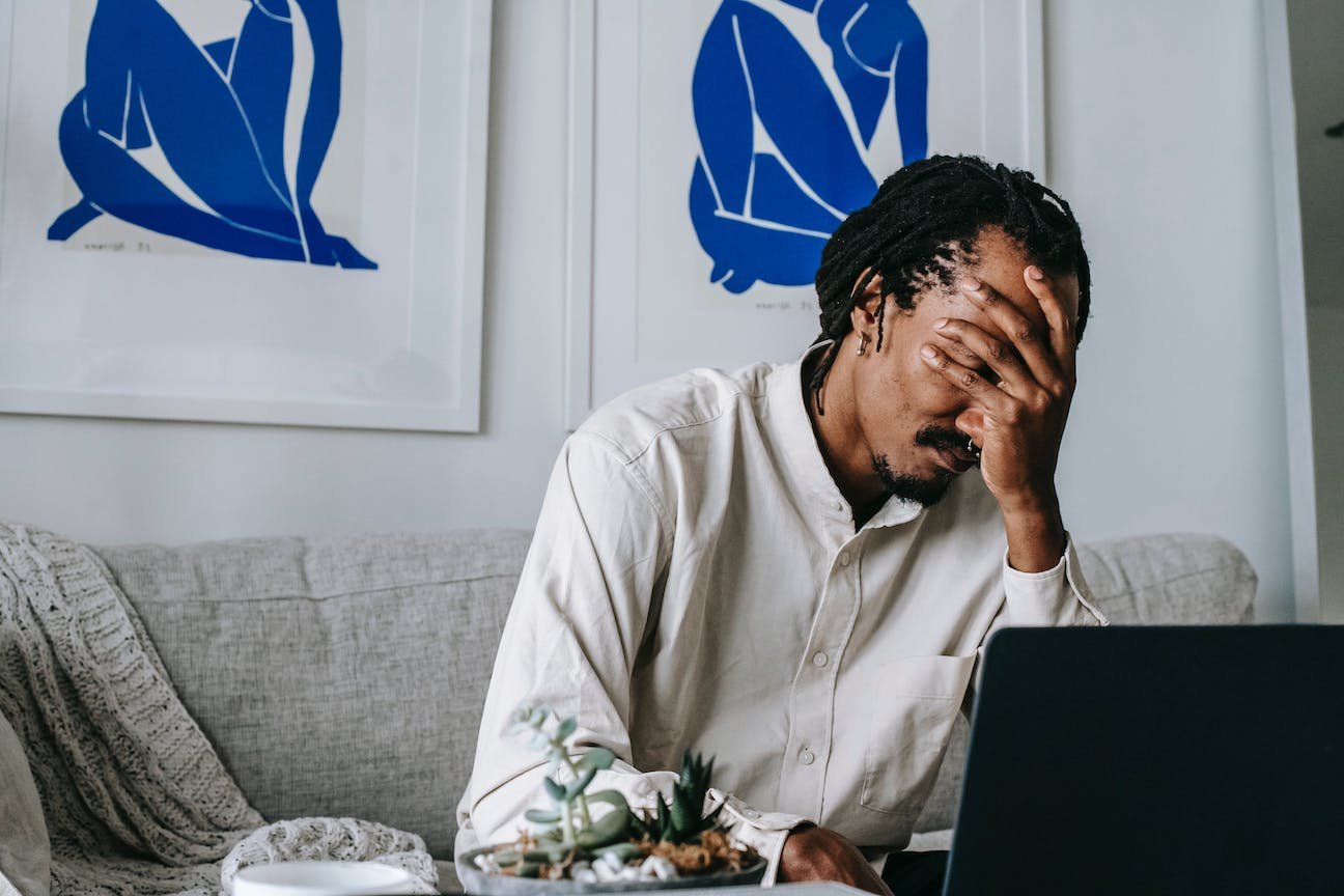 man-sits-on-couch-in-front-of-laptop-dealing-with-feelings-of-failure