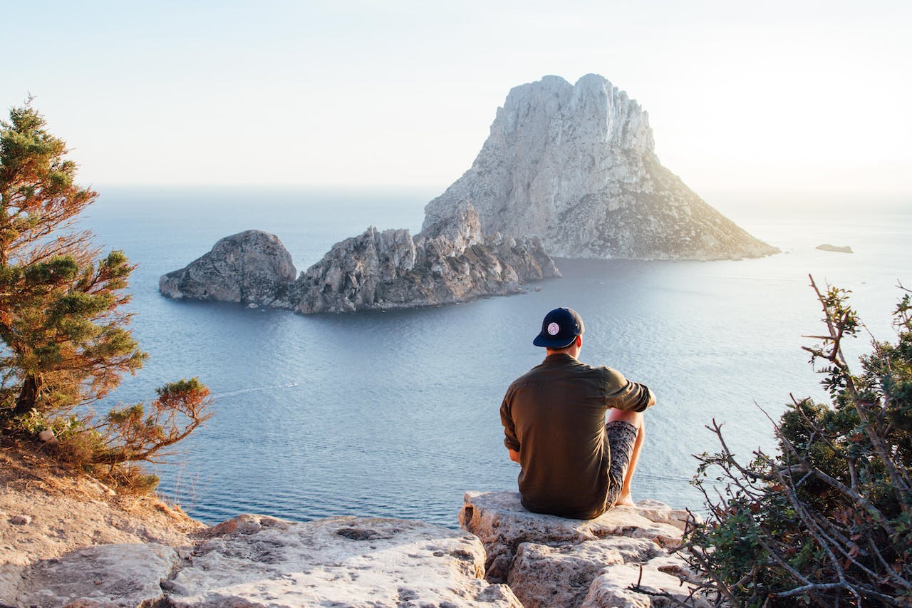 rear-view-of-man-sitting-on-rock-by-sea