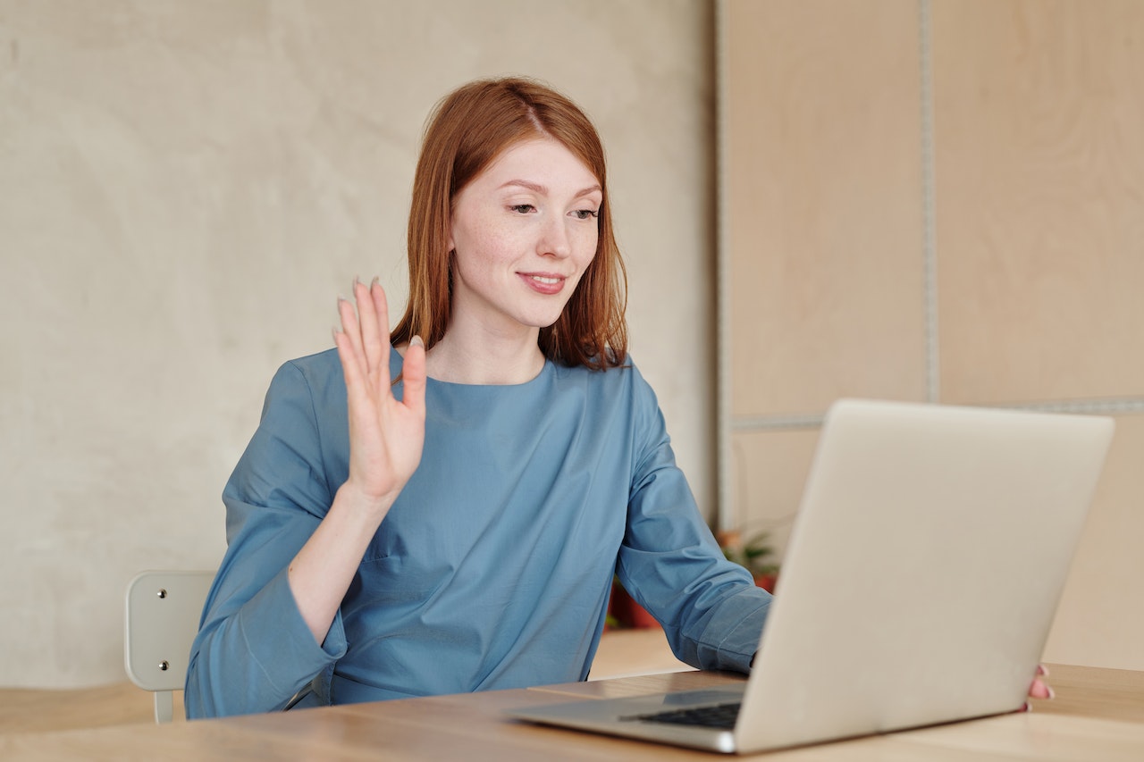 redhea-woman-waving-at-her-laptop-camera-on-virtual-job-interview-what-to-wear-to-a-job-interview
