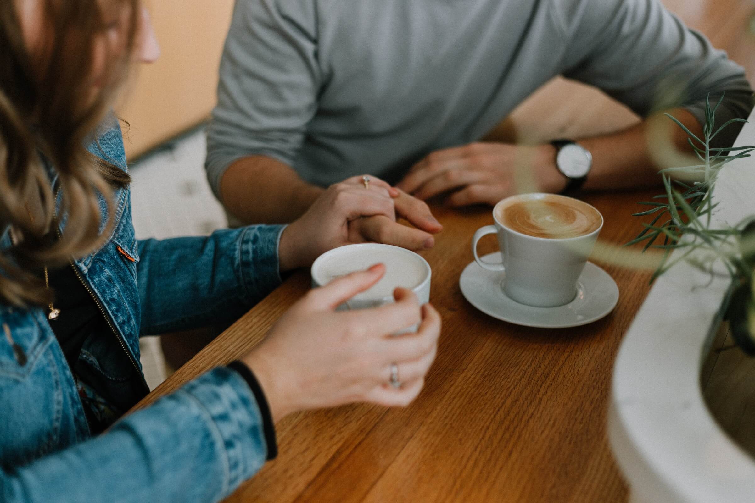 two peoples hands and mugs of coffee