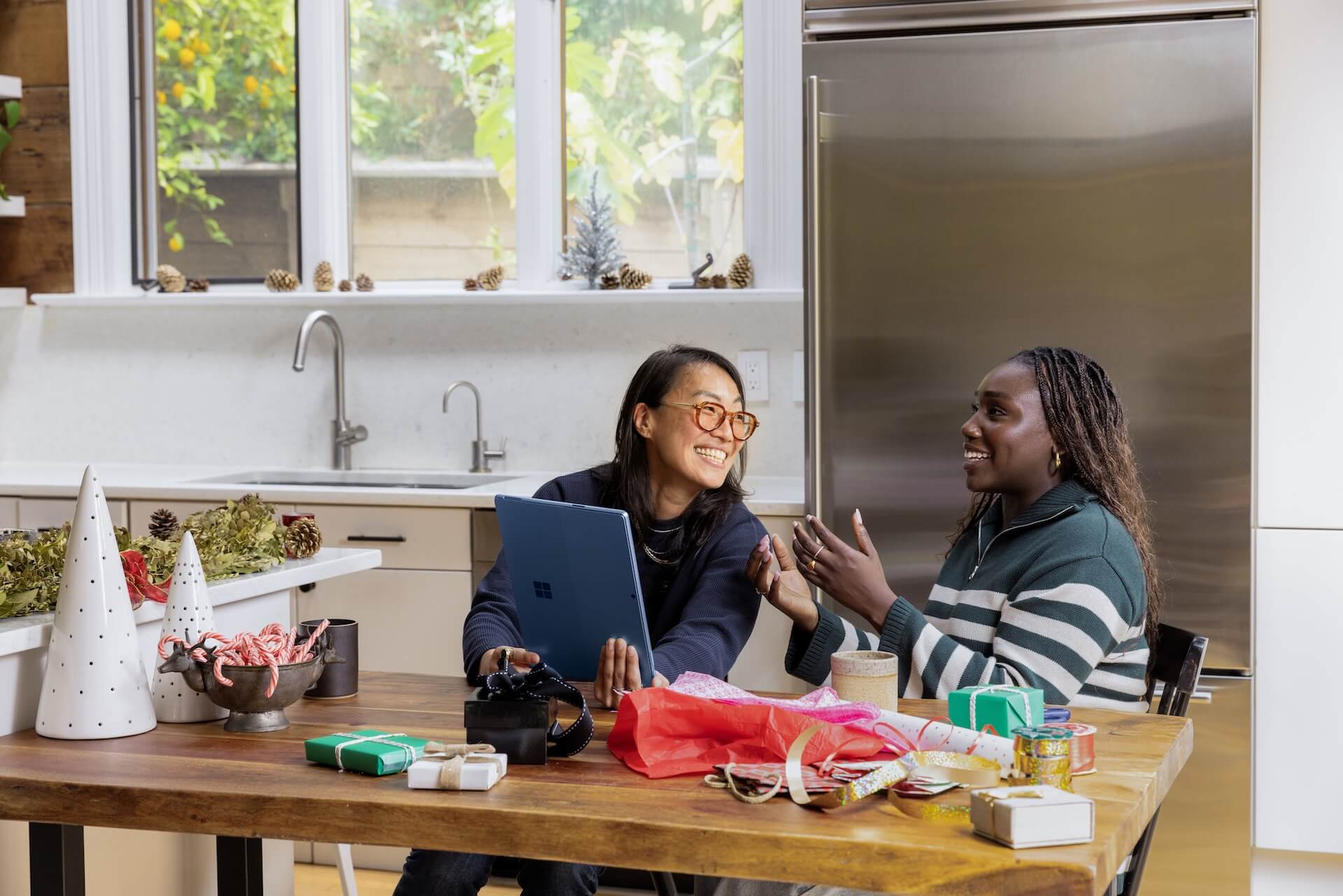 two women talking smiling in kitchen with computer and wrapping supplies