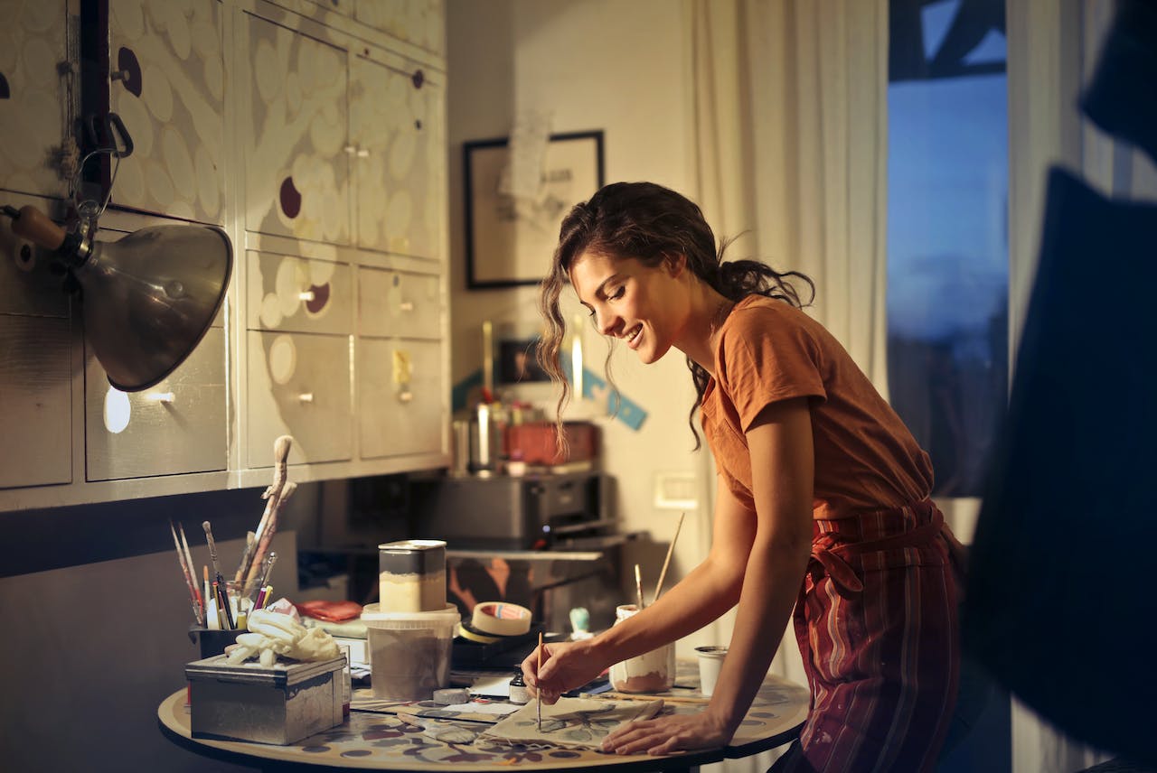 woman-painting-while-smiling-and-standing-by-the-table