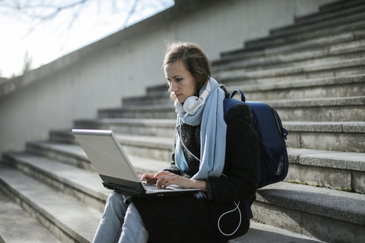 woman-sitting-in-stairs-outdoors-taking-online-class-with-laptops-and-headphones-entrepreneurial-skills