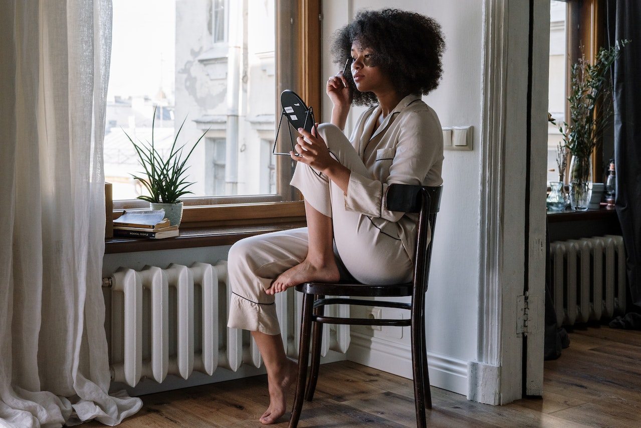 woman-sitting-on-chair-in-front-of-her-window-in-the-morning-doing-her-makeup-how-to-stay-positive