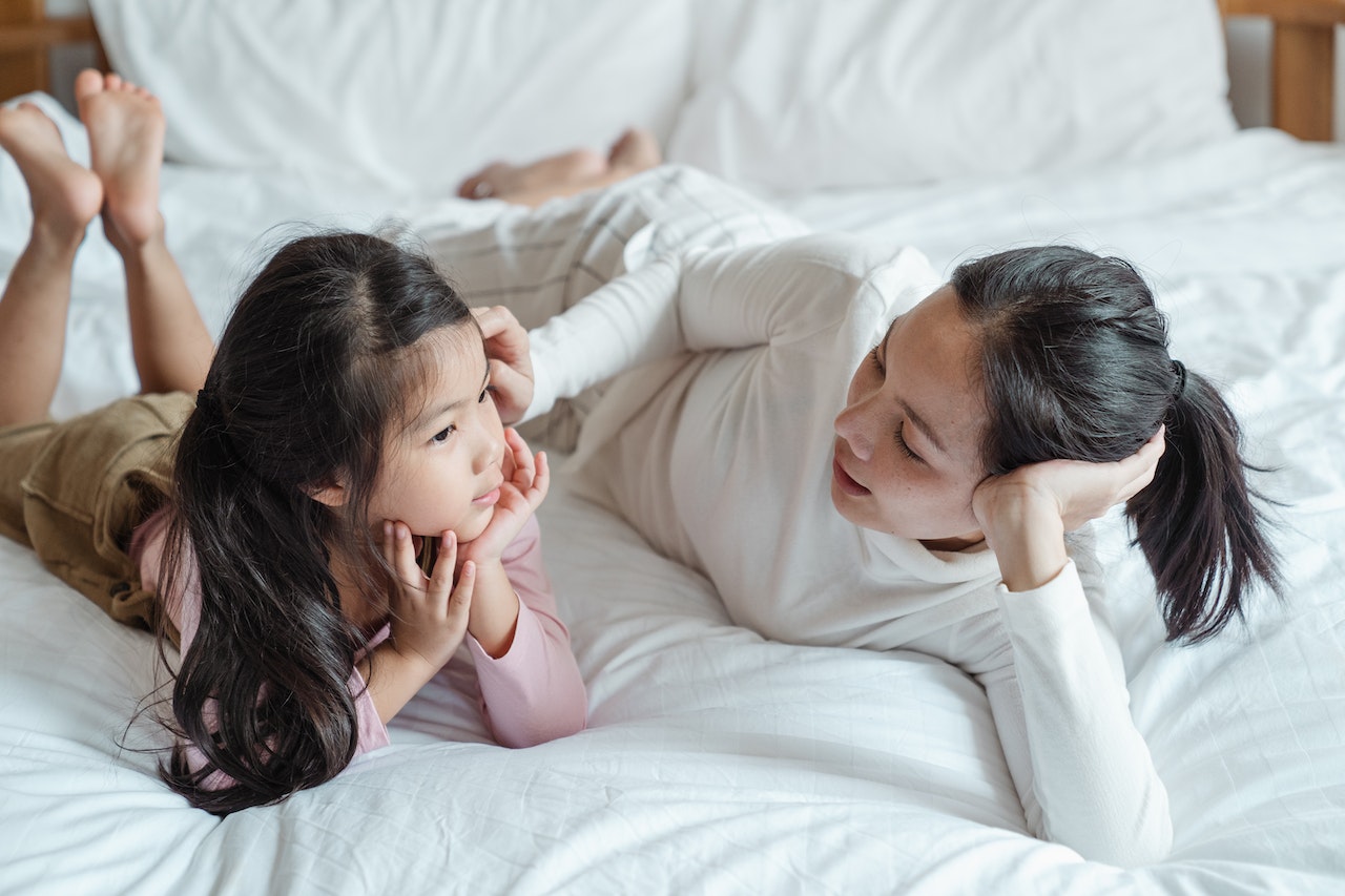 woman-talking-to-her-toddler-daughter-laying-in-bed-positive-parenting