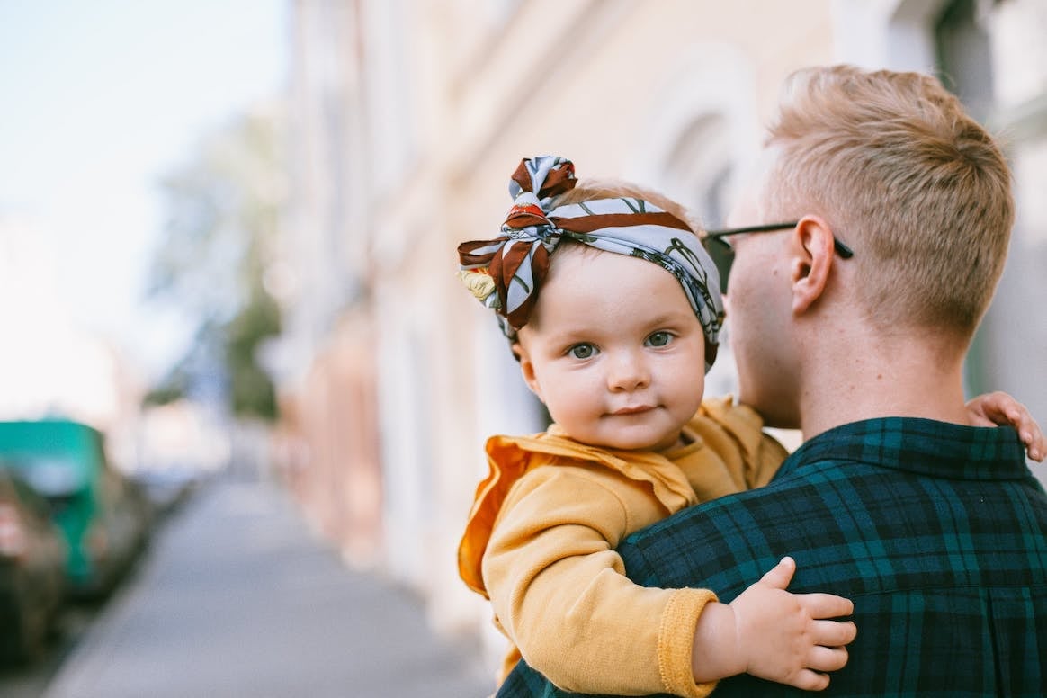man holds baby girl over shoulder-Paternity Leave in the US