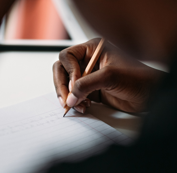 person of color's hands writing in pencil on paper