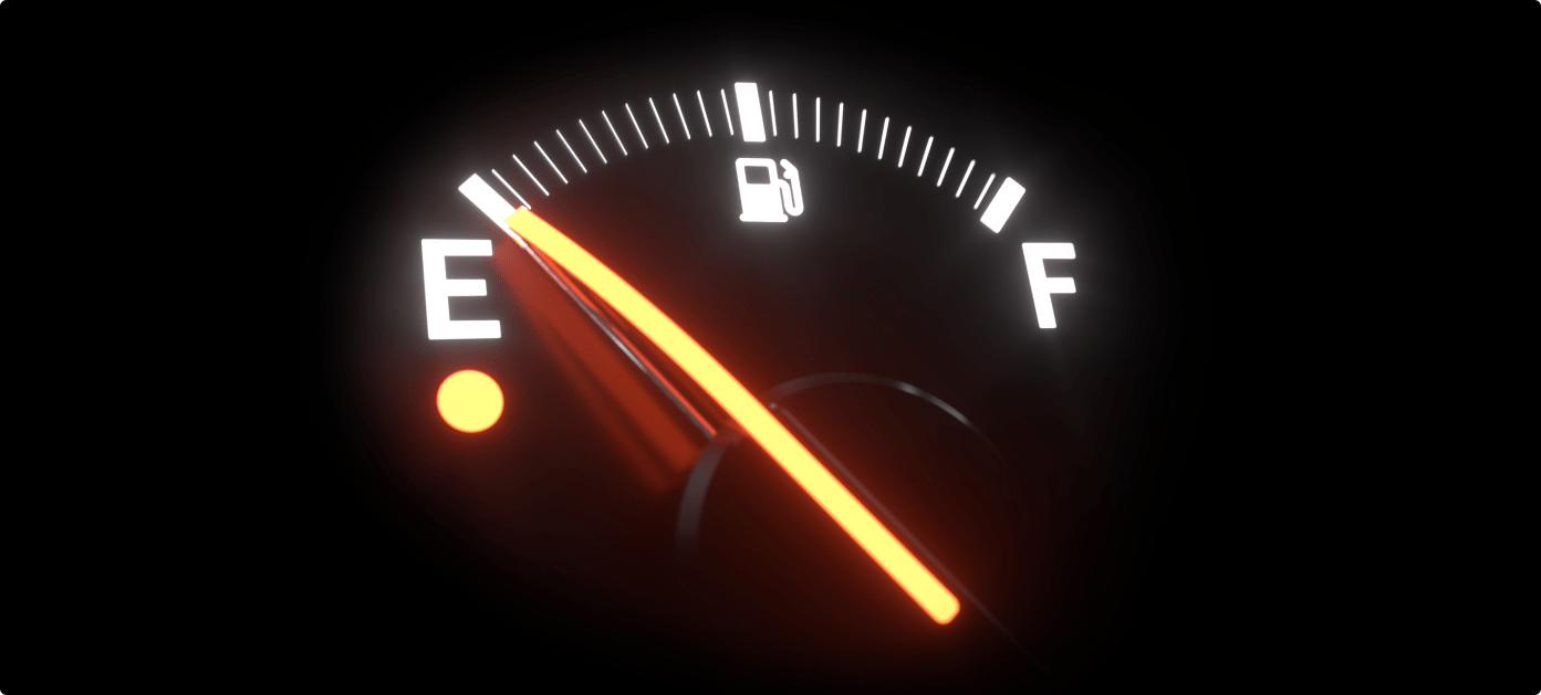 A close-up of a car fuel gauge showing the needle near empty with a low-fuel warning light illuminated.