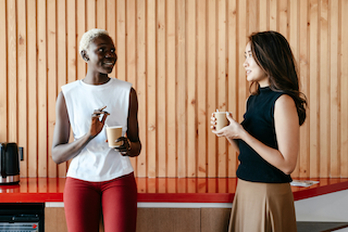 two-women-talk-while-holding-coffee-in-an-office-break-room